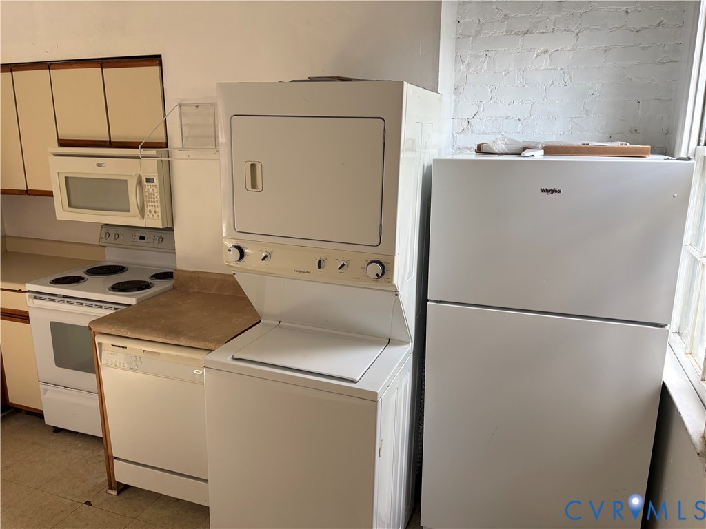 Kitchen featuring light-toned cabinetry, built-in microwave, electric range, dishwasher, and stackable laundry unit