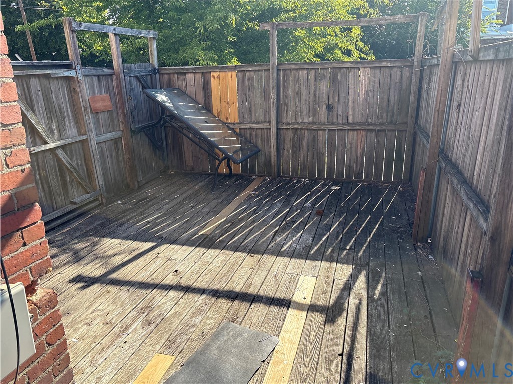 Enclosed outdoor deck featuring horizontal wood-plank flooring and a vertical wood privacy fence