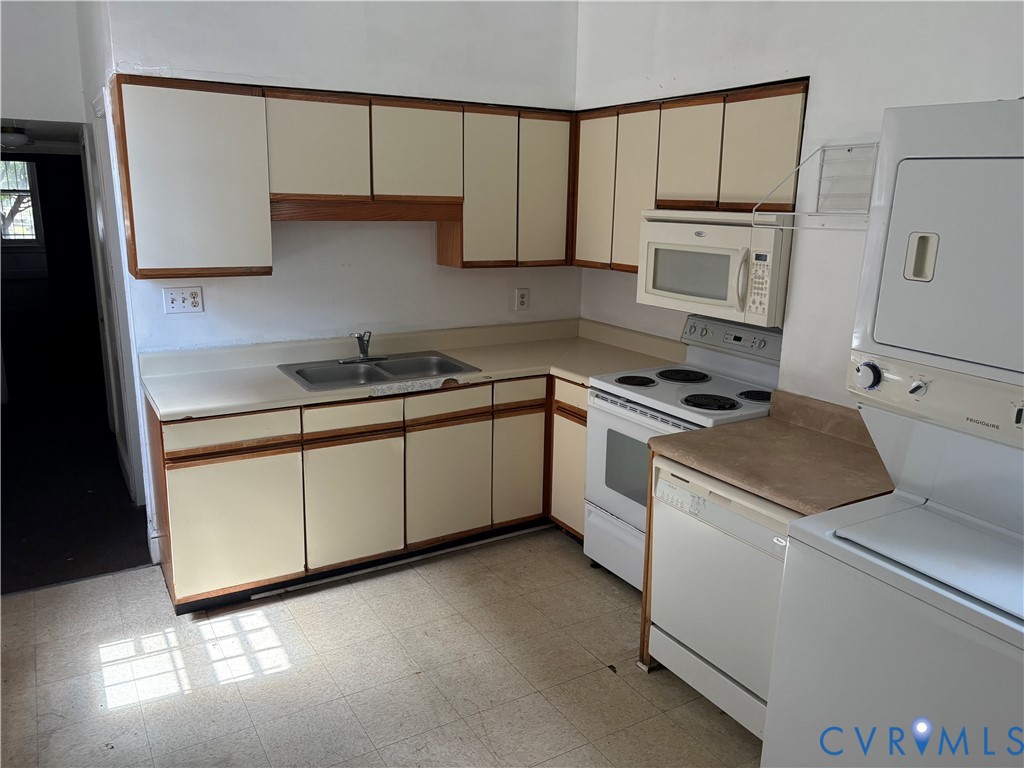 Kitchen featuring cream-toned cabinetry with wood trim, dual-basin stainless steel sink, built-in microwave, and an integrated stacked laundry unit