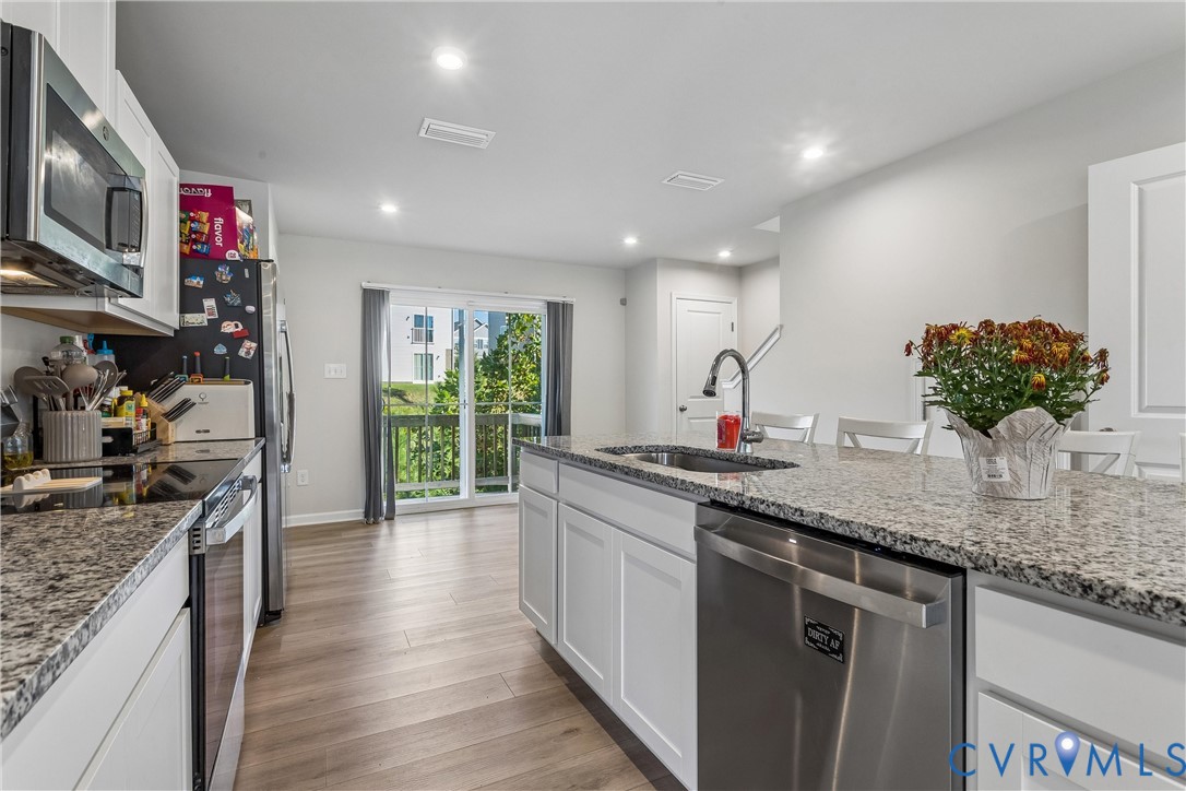 Kitchen featuring a center island with an undermount sink, stone-finish countertops, white cabinetry, stainless steel appliances, and wood-finish flooring