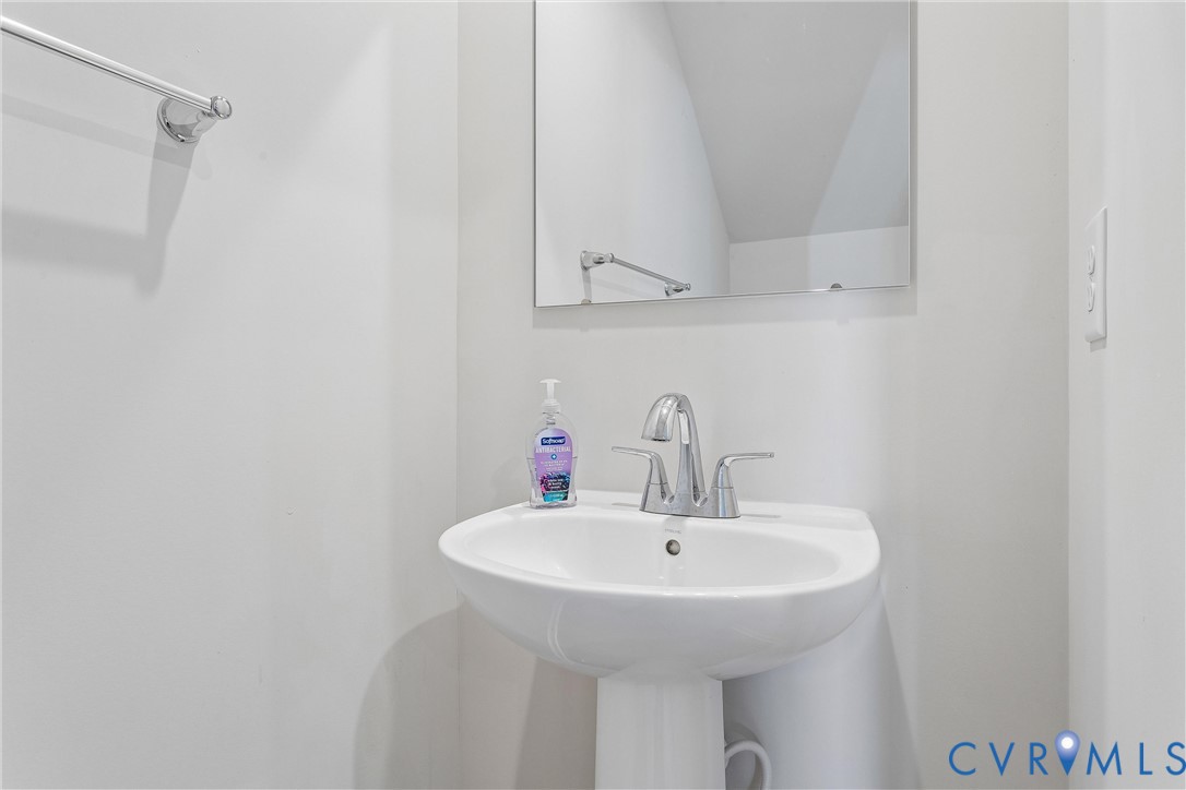White pedestal sink featuring a chrome dual-handle faucet, frameless wall-mounted mirror, and chrome towel bar