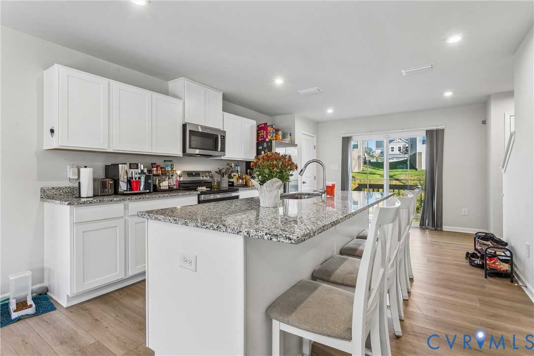 Kitchen featuring white cabinetry, stone-surface countertops, center island with integrated sink, stainless steel appliances, and wood-finish flooring