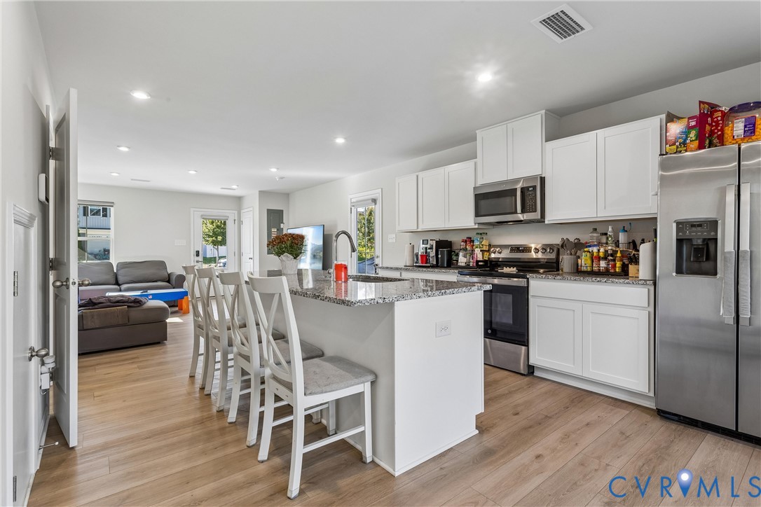 Kitchen featuring white cabinetry, stone-surface countertops, central island, wood-finish flooring, and stainless-steel appliances