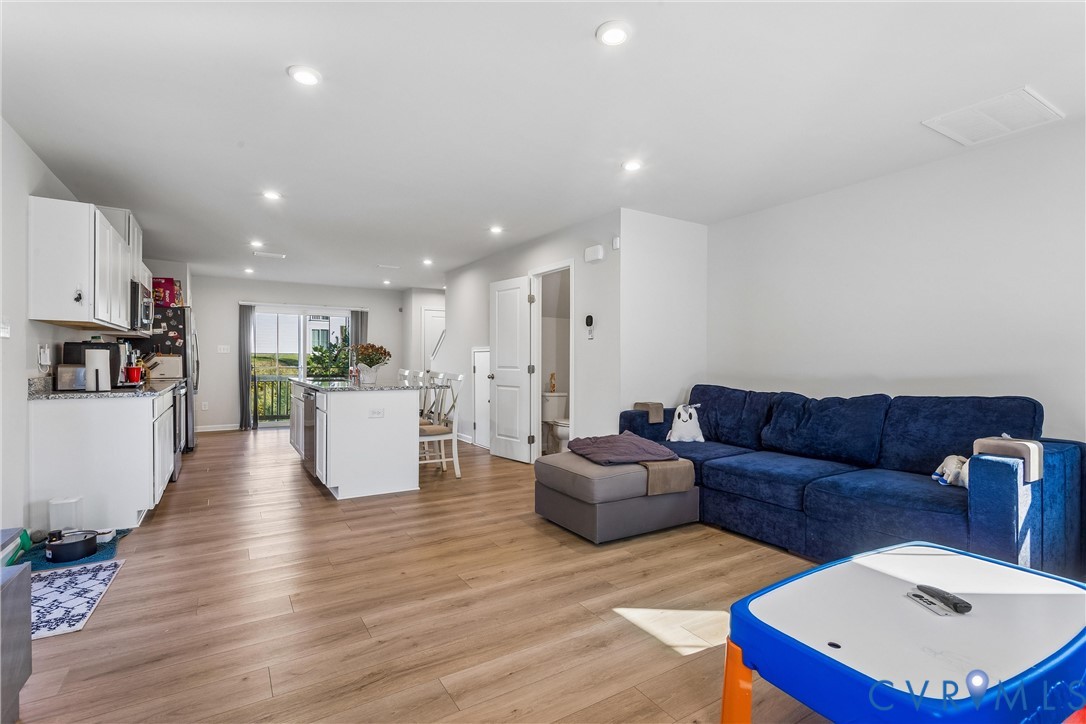 Open-concept interior featuring wood-finish flooring, recessed lighting, and a kitchen equipped with white cabinetry and an island