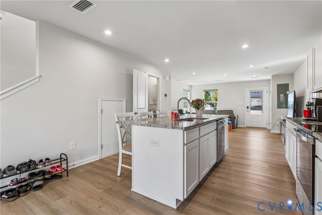 Kitchen featuring a stone-topped island with an integrated stainless-steel sink, shaker-style white cabinetry, wood-finish flooring, recessed lighting, and stainless-steel appliances