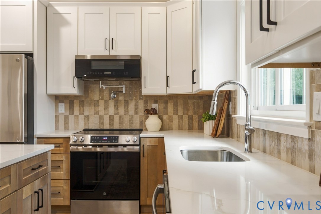 Kitchen featuring shaker-style cabinetry, quartz countertops, tile backsplash, stainless steel appliances, and a wall-mounted pot filler