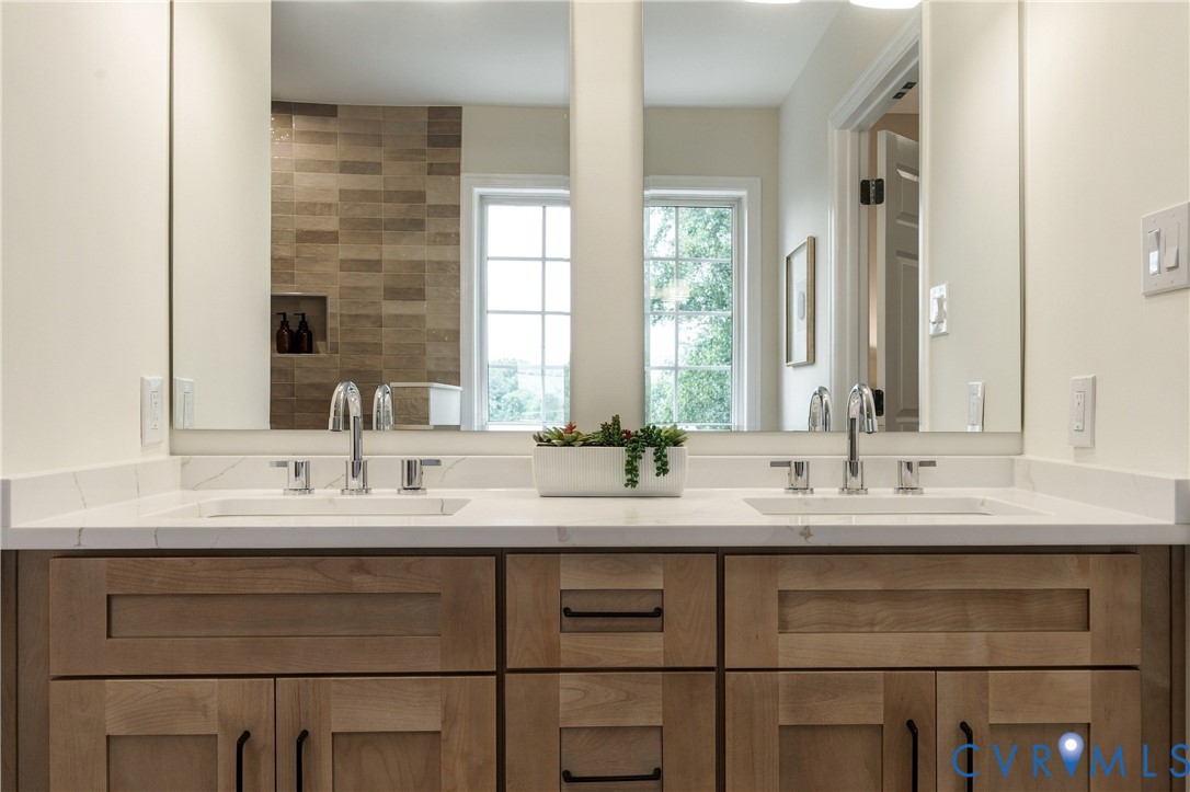 Double vanity featuring wood-finish cabinetry, rectangular under-mount sinks, a solid-surface countertop, and polished chrome widespread faucets