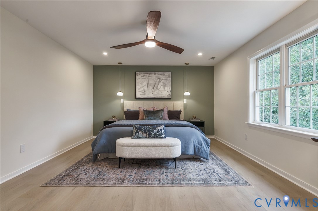 Wood-finish flooring, multi-pane window, ceiling fan with integrated lighting, dual pendant fixtures, and an accent wall