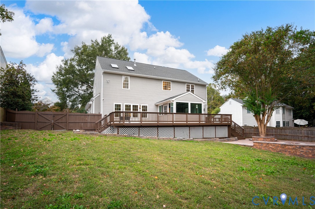 Rear exterior featuring a grey-sided two-story home, elevated wooden deck with lattice skirting, skylights, enclosed sunroom, and privacy wood fencing