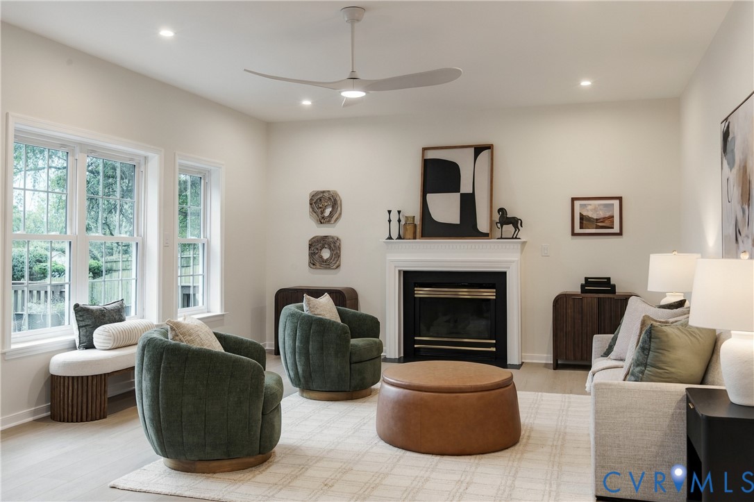 Living area featuring a fireplace with a white mantel surround, large multi-pane windows, recessed lighting, a modern ceiling fan, and light-toned flooring