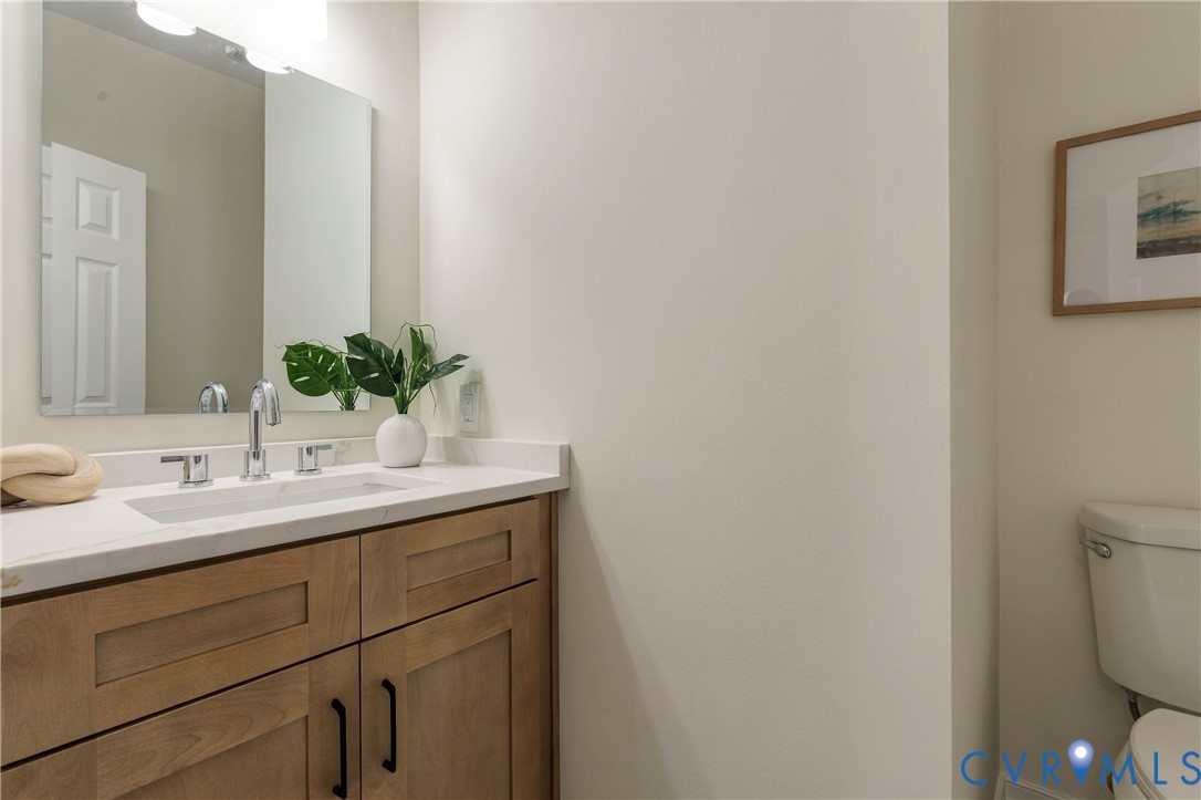 Bathroom featuring a wood-finish vanity with shaker-style cabinetry, white countertop with an integrated rectangular sink, chrome widespread faucet, large frameless wall mirror, and high-mounted vanity lighting