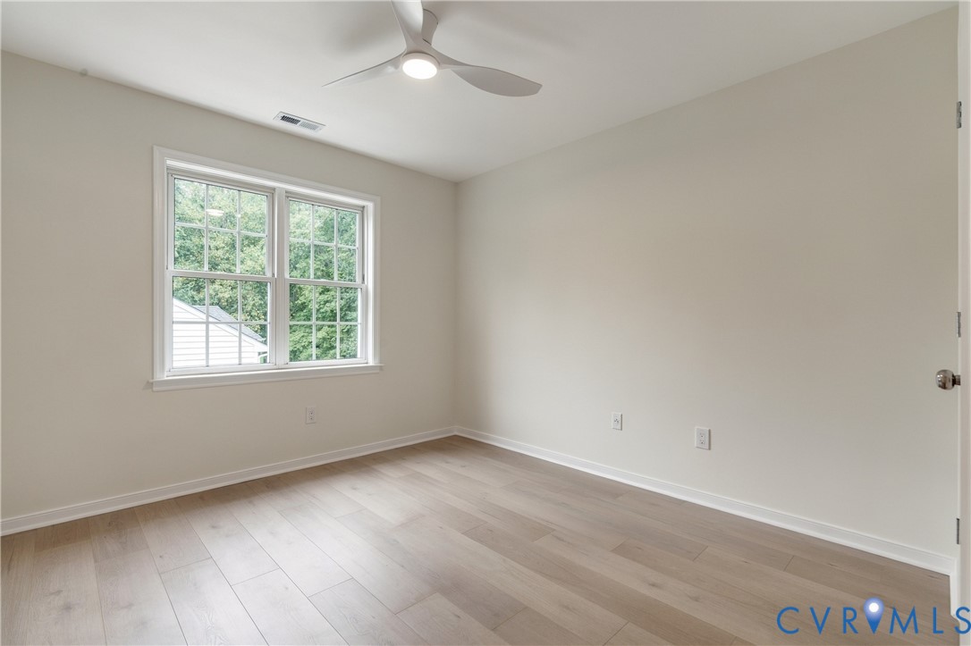 Neutral-toned room featuring wood-finish flooring, a white three-blade ceiling fan with integrated lighting, and a double-hung window with muntin grids
