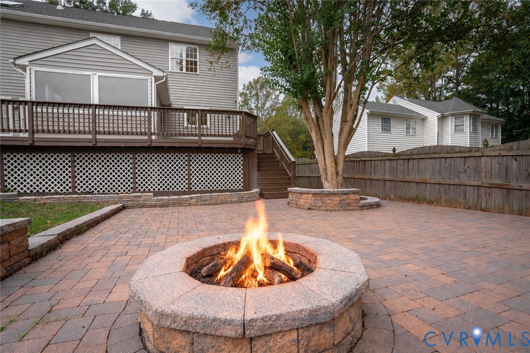 Paver patio featuring a circular stone fire pit, tiered wooden deck with lattice skirting, and stone retaining walls