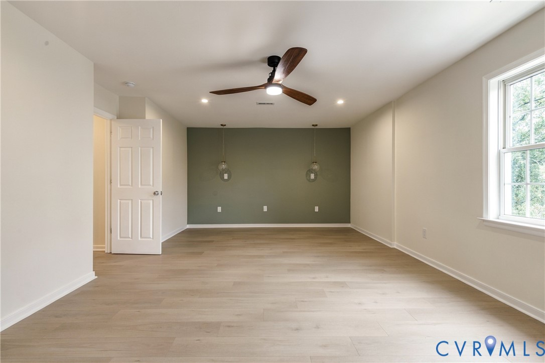 Room featuring wood-finish flooring, accent wall, ceiling fan with integrated lighting, and dual glass pendant light fixtures