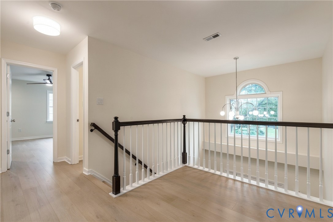 Landing area featuring wood-finish flooring, a decorative arched window, a multi-arm chandelier, and a staircase with white balusters and dark wood-finish handrails