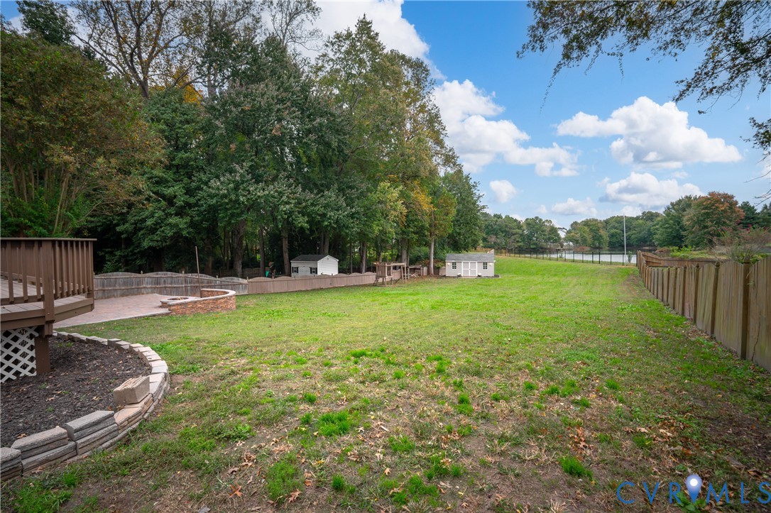 Expansive backyard featuring a tiered wooden deck, stone-bordered landscape beds, a brick retaining wall, and peripheral wood fencing