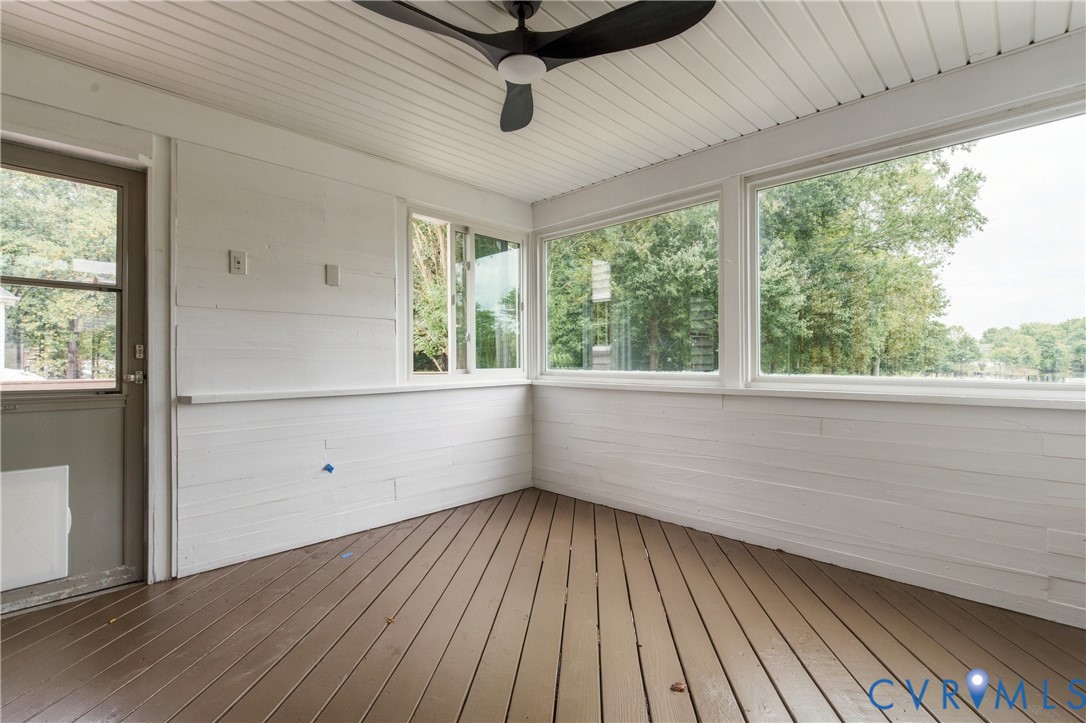 Enclosed porch featuring wood-finish flooring, white horizontal wall paneling, ceiling fan, and large windows