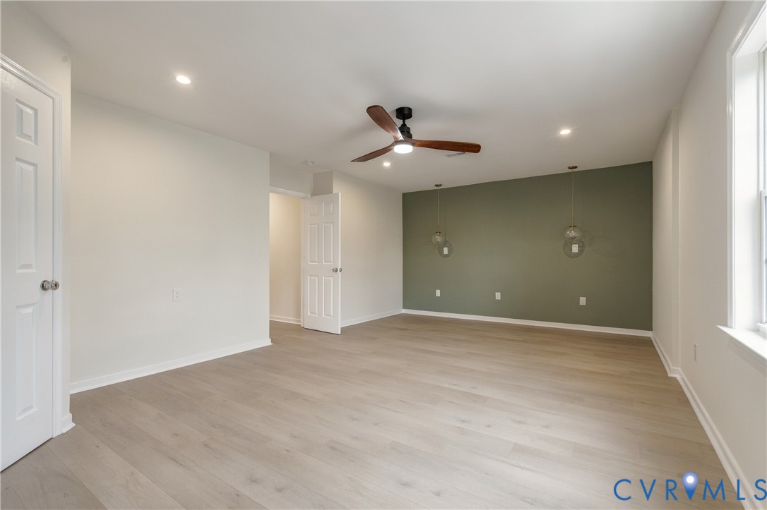 Light-toned wood-finish flooring, accent wall, recessed lighting, ceiling fan with integrated light, and two suspended glass pendant lights