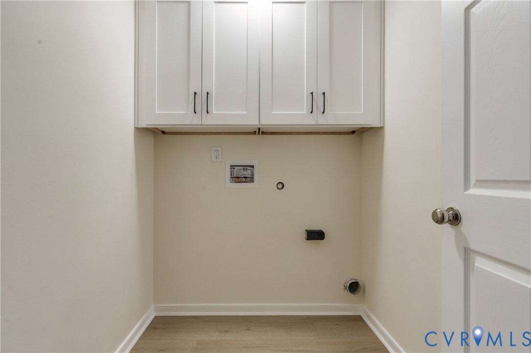 Utility area featuring white shaker-style wall cabinetry with dark hardware and wood-finish flooring