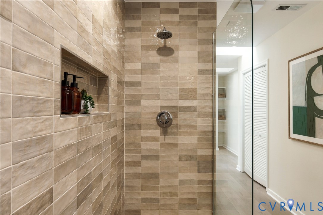 Walk-in shower featuring textured ceramic wall tile, a built-in recessed wall niche, a glass enclosure, and metallic fixed-head plumbing fixtures
