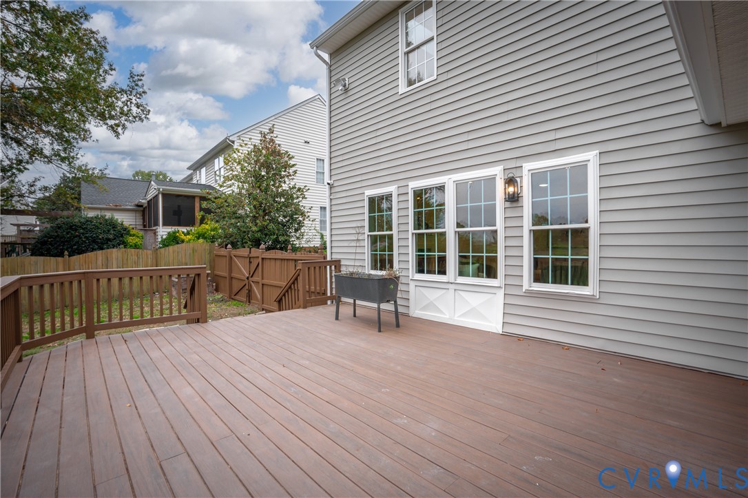 Spacious rear deck featuring horizontal composite decking, wood-finish railing, light-grey siding, multi-pane windows, and a wood privacy fence