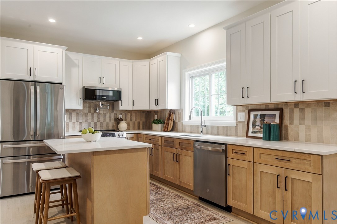 Kitchen featuring white upper cabinetry, natural wood-finish lower cabinetry, stone-tile backsplash, stainless steel appliances, and a central island with a solid surface countertop