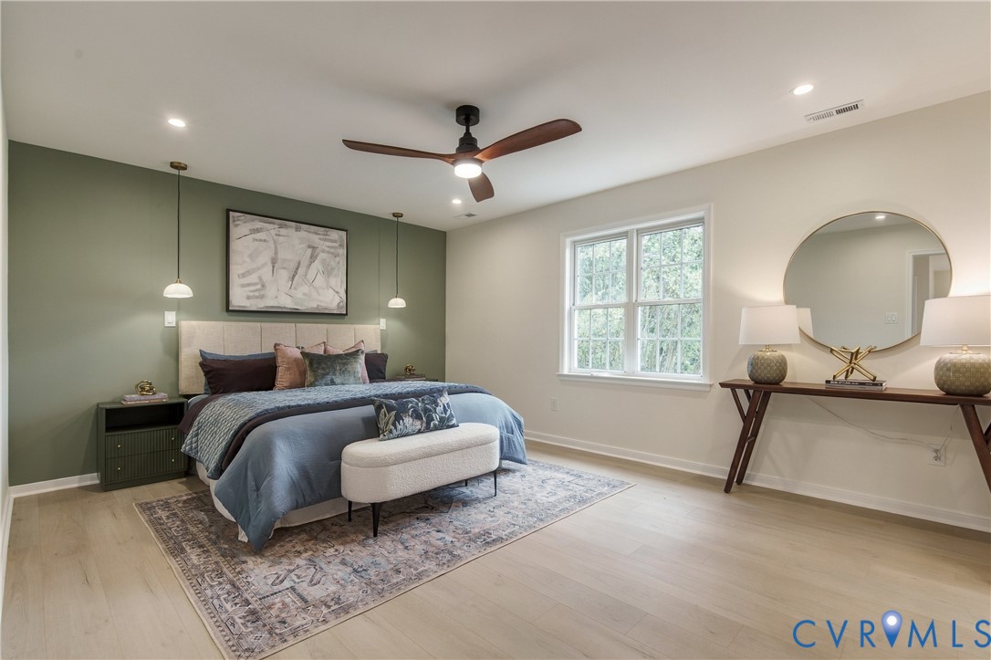 Room featuring light wood-finish flooring, a sage green accent wall, dual pendant light fixtures, and a ceiling fan