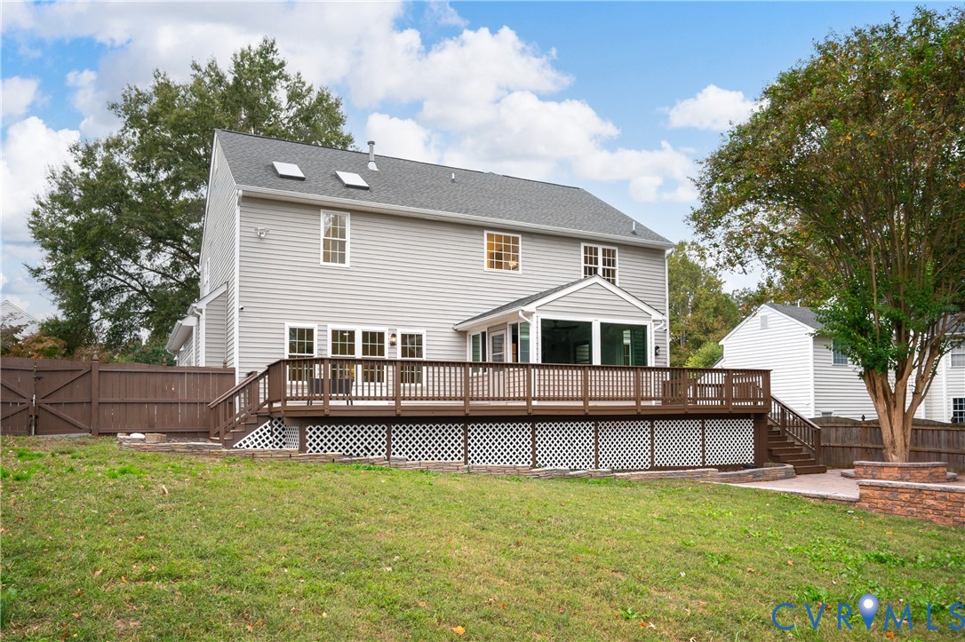 Rear exterior featuring gray siding, a raised wood deck with lattice skirting, an enclosed sunroom, two roof skylights, and perimeter wood fencing