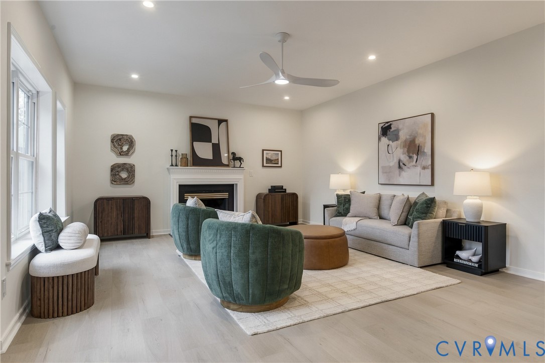 Living area featuring light-toned wood-finish flooring, recessed lighting, a modern ceiling fan, and a fireplace with a decorative mantel
