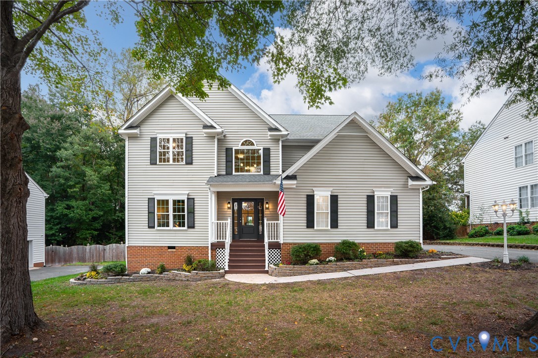 Two-story exterior featuring light-toned horizontal siding, a partial brick facade, a covered front entry with steps, decorative window shutters, and a stone-lined front landscape border