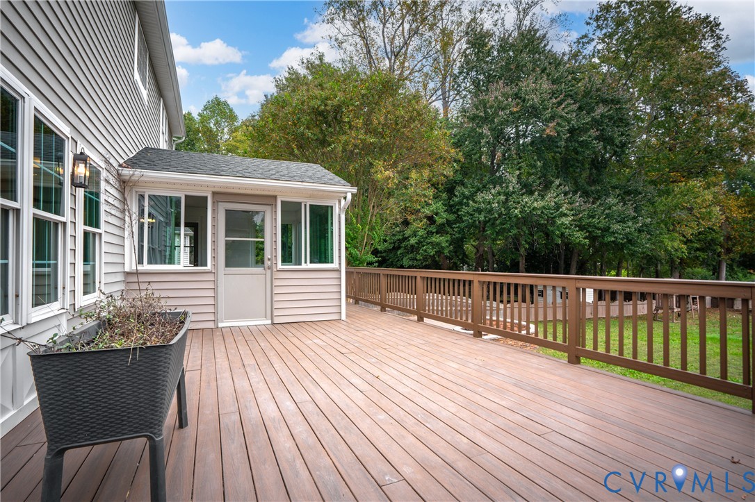 Expansive wood-finish deck featuring a full-width railing, light-filled sunroom addition, exterior wall-mounted lighting, and siding exterior