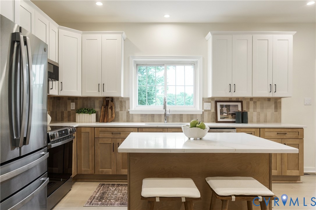 Kitchen featuring two-tone shaker-style cabinetry, a central island with a solid-surface countertop, stainless steel appliance package, and a tile backsplash Kitchen featuring two-tone shaker-style cabinetry, a central island with a solid-surface countertop, stainless steel appliance package, and a tile backsplash
