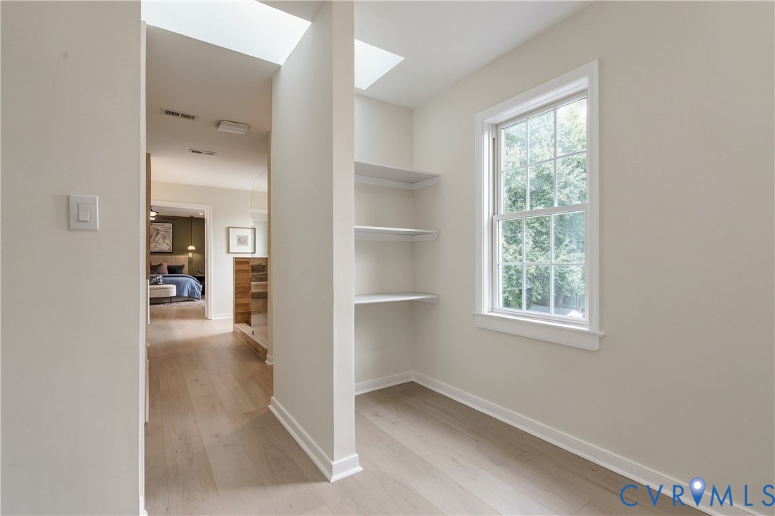 Interior space featuring wood-finish flooring, dual skylights, built-in shelving, and a multi-pane window