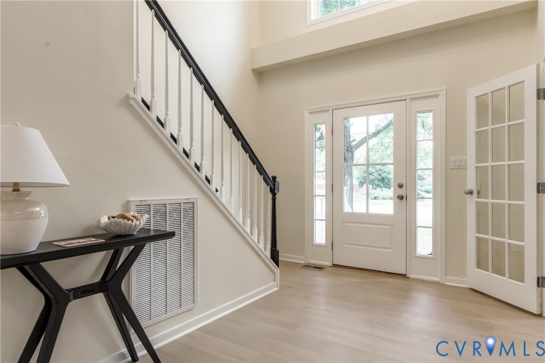 Foyer featuring high ceilings, wood-finish flooring, a staircase with a black handrail and white balusters, a multi-pane glass entry door with side lights, and a French-style glass pane door Foyer featuring high ceilings, wood-finish flooring, a staircase with a black handrail and white balusters, a multi-pane glass entry door with side lights, and a French-style glass pane door