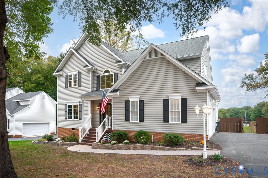 Two-story exterior featuring horizontal siding, brick veneer foundation, multi-gabled roofline, decorative shutters, and an elevated front porch