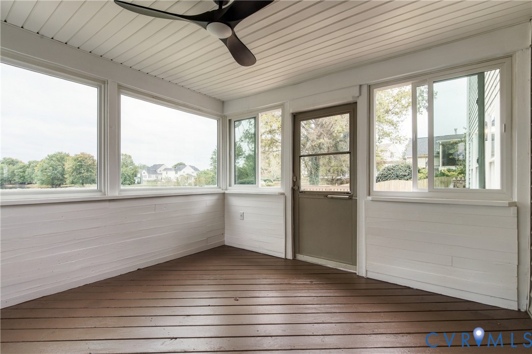 Enclosed porch featuring wood-finish decking, white horizontal shiplap wall paneling, large sliding windows, and an overhead ceiling fan