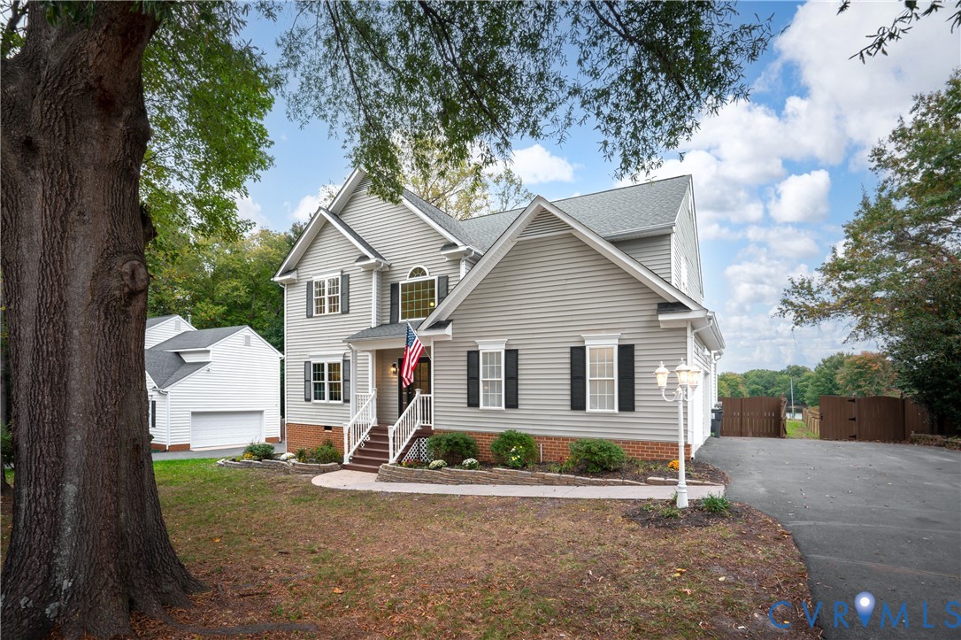 Two-story home with gray horizontal siding, brick foundation accents, covered entryway, asphalt shingle roof, and detached garage