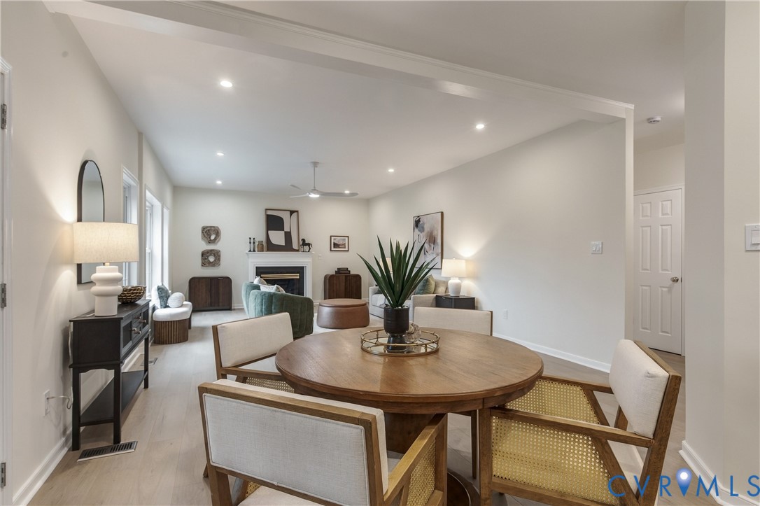 Open-concept interior featuring light-toned wood-finish flooring, recessed lighting, and a central fireplace with a classic mantel