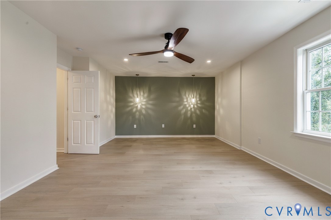 Interior room featuring wood-finish flooring, a multi-tone accent wall, dual wall-mounted pendant lights, a ceiling fan with integrated lighting, and recessed ceiling lights