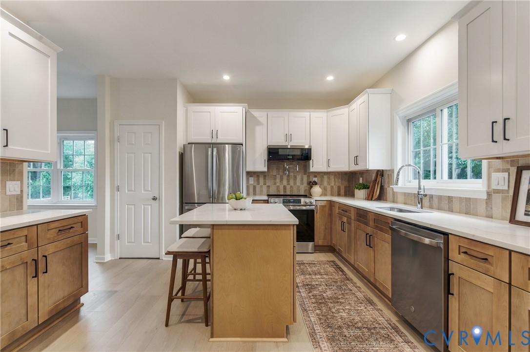 Kitchen featuring two-tone shaker-style cabinetry, quartz countertops, stainless steel appliances, a center island with counter seating, and wood-finish flooring Kitchen featuring two-tone shaker-style cabinetry, quartz countertops, stainless steel appliances, a center island with counter seating, and wood-finish flooring