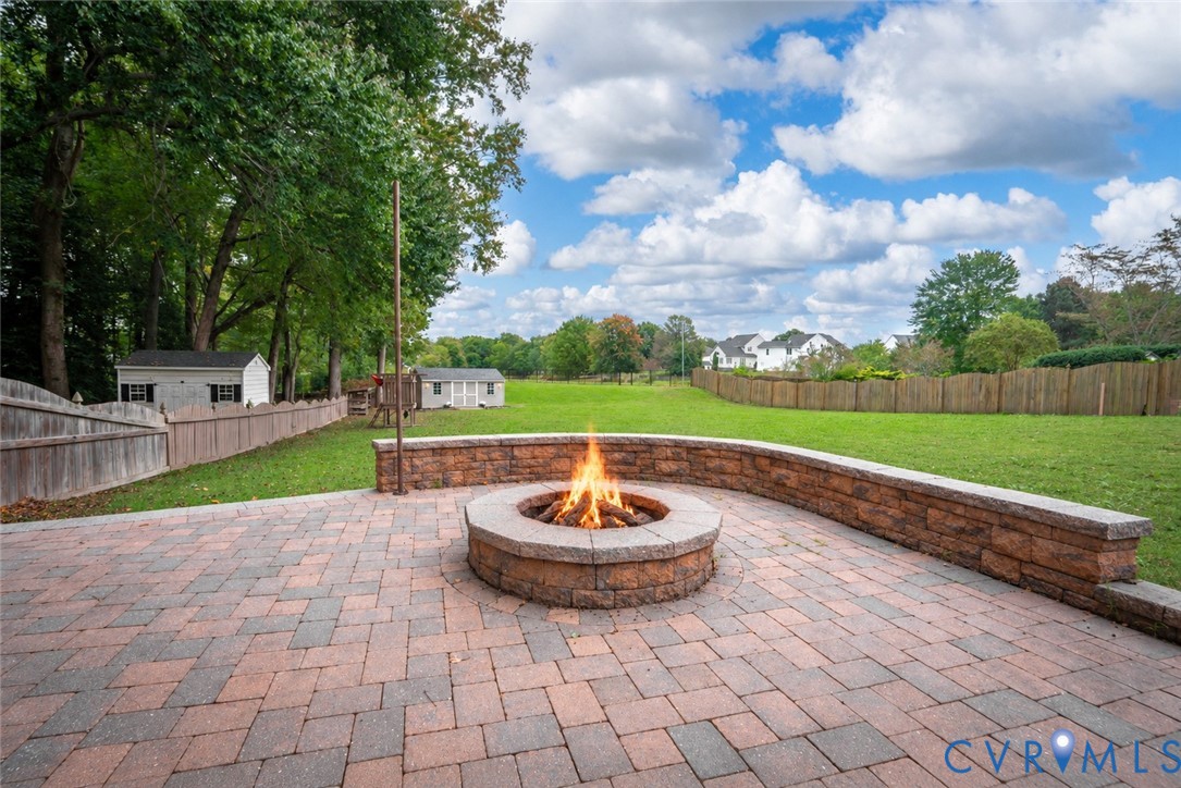 Paver patio featuring a circular stone fire pit and a curved retaining wall bordering a fenced-in grassy lawn