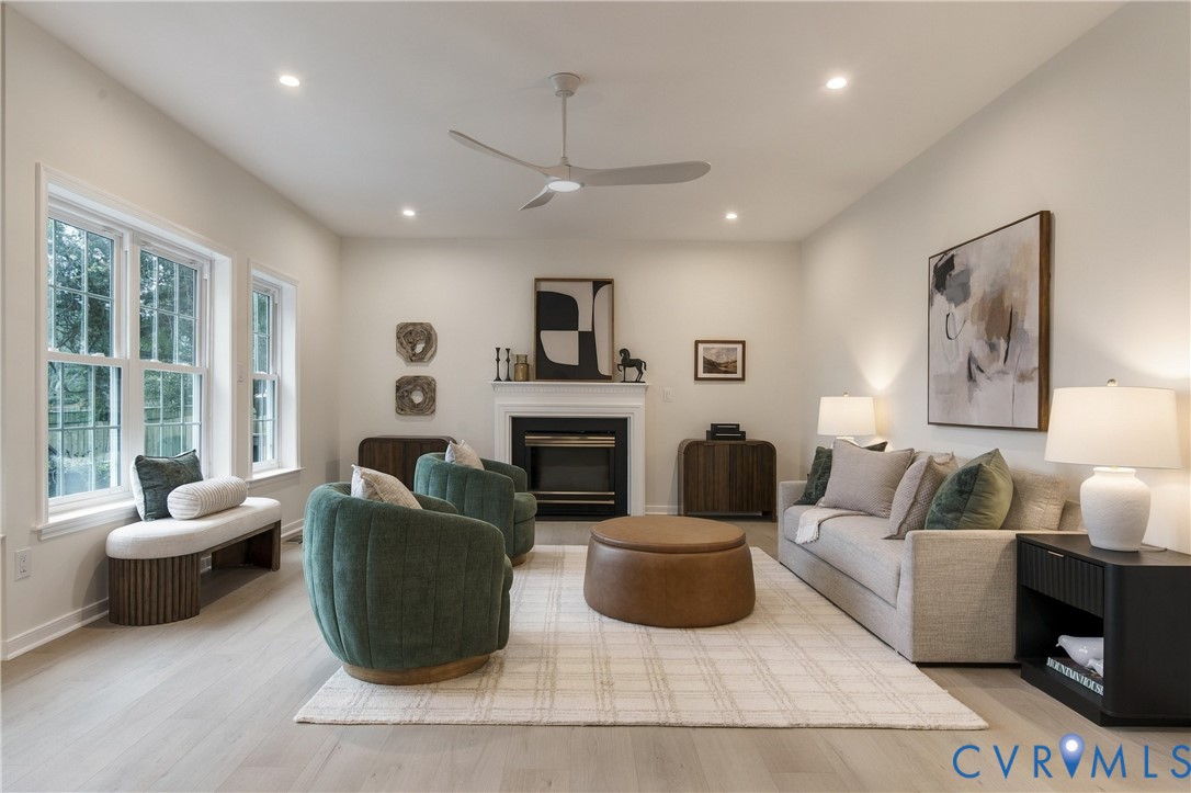 Living area featuring wood-finish flooring, a fireplace with a white mantel, recessed lighting, a modern ceiling fan, and double-hung windows