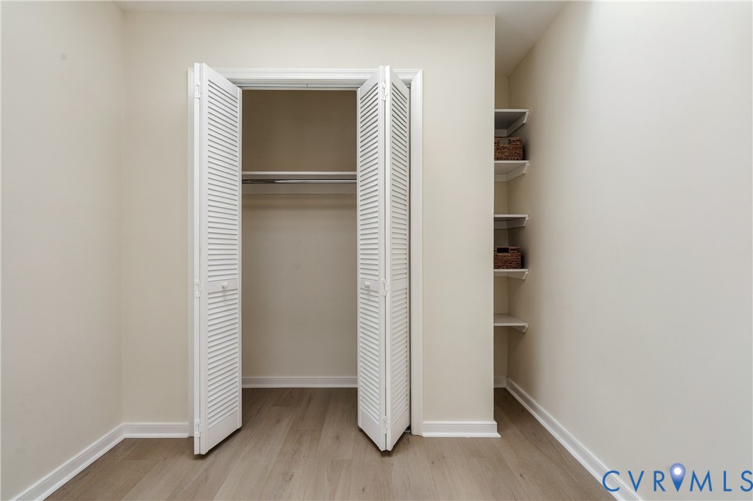 Closet featuring white louvered bifold doors, integrated hanging rod, wood-finish flooring, and built-in wall shelving