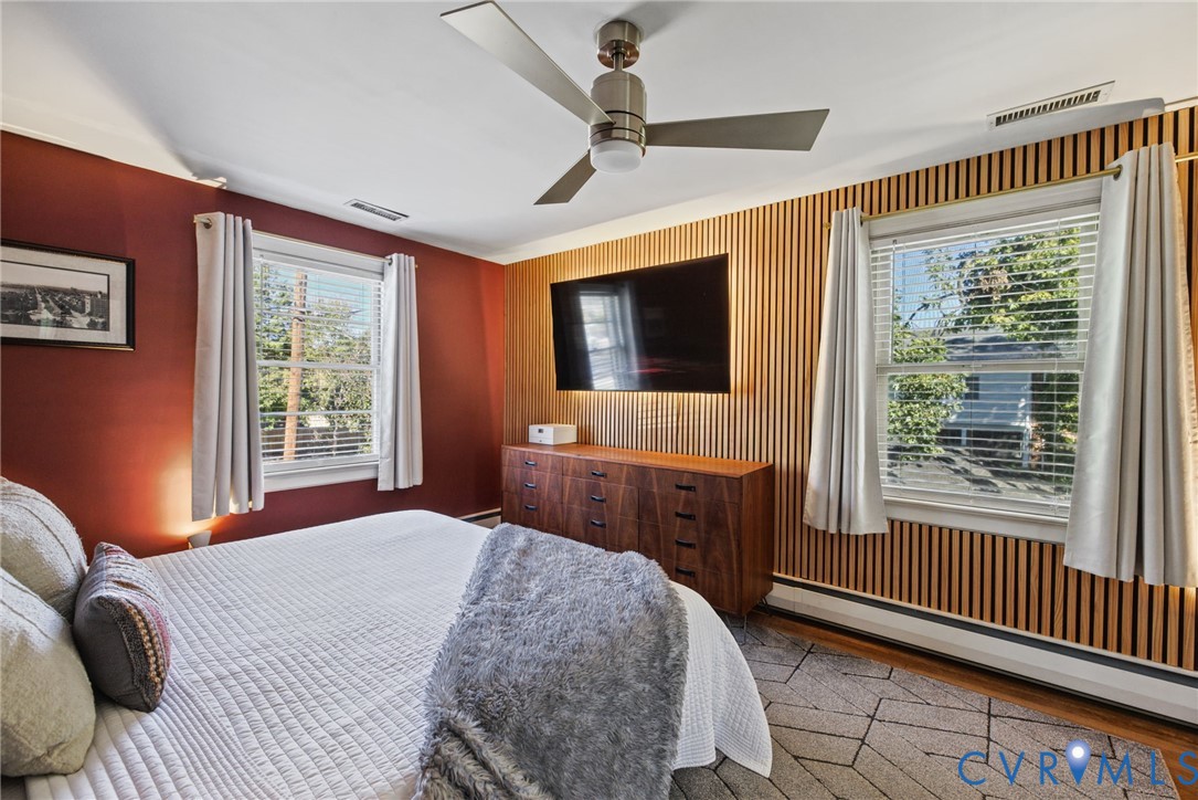 Bedroom featuring an accent wall with vertical wood slat paneling, dual windows with blinds, and a brushed nickel ceiling fan with integrated lighting