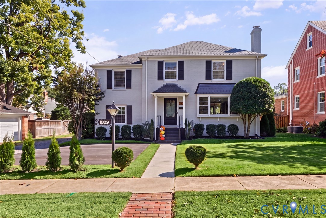 Painted brick exterior featuring dark shutters, a covered front entryway, a chimney, and a landscaped front lawn Painted brick exterior featuring dark shutters, a covered front entryway, a chimney, and a landscaped front lawn