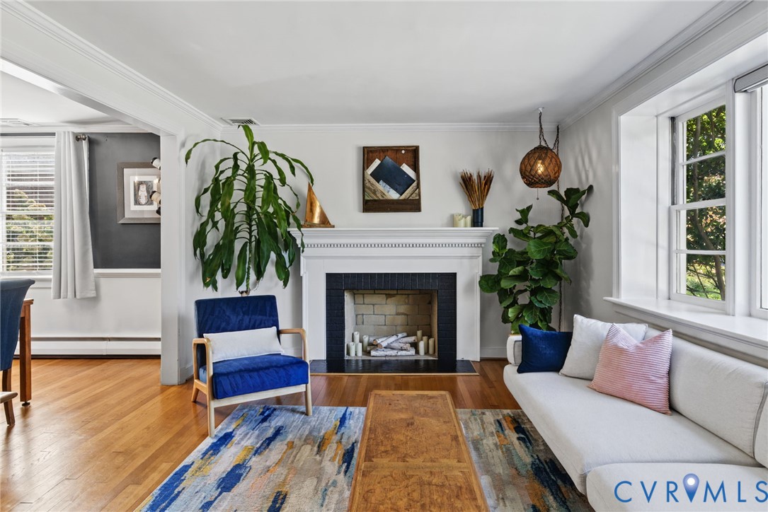 Living area featuring wood-finish flooring, a traditional fireplace with a white mantel and black surround, multi-pane windows, and crown molding Living area featuring wood-finish flooring, a traditional fireplace with a white mantel and black surround, multi-pane windows, and crown molding