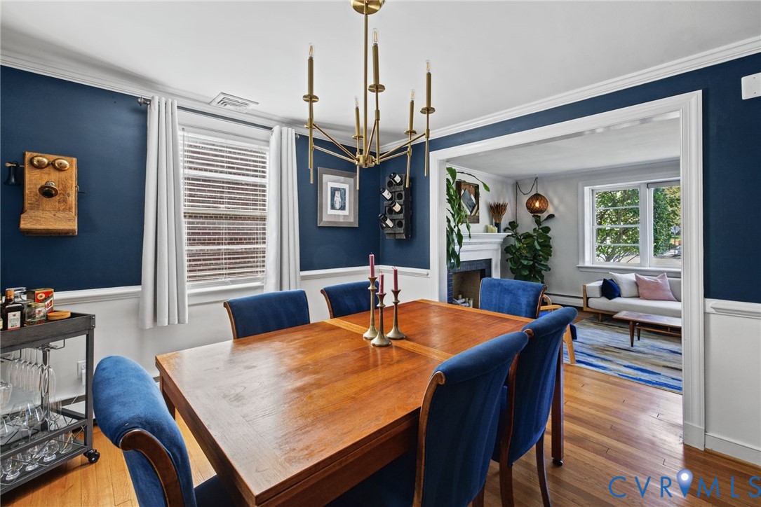 Dining area featuring wood-finish flooring, chair rail molding, a multi-arm candle-style chandelier, and a fireplace with a wood mantel
