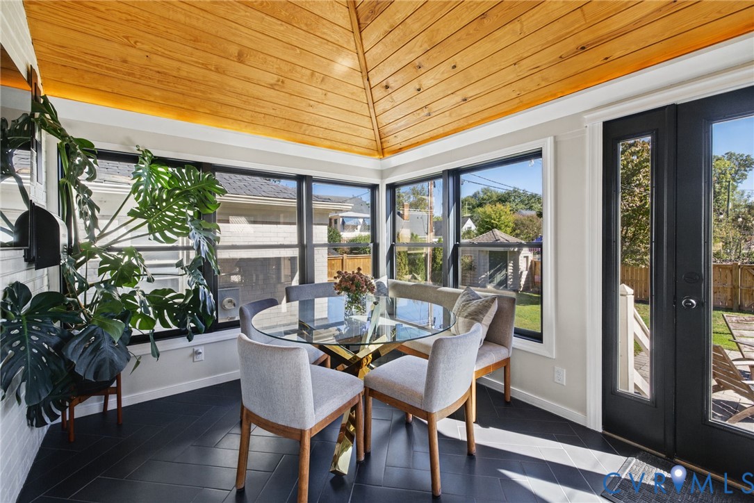 Sunroom featuring a vaulted natural wood-plank ceiling, dark herringbone-patterned flooring, wrap-around windows with black framing, and a full-lite glass exterior door