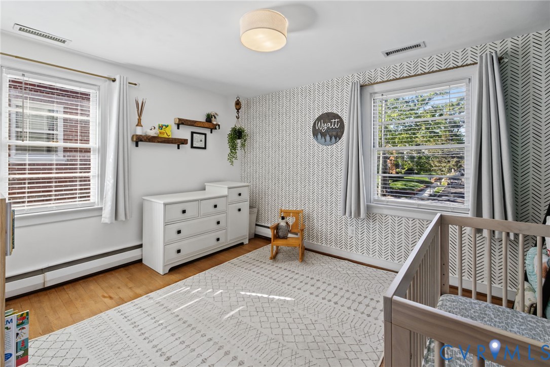 Bedroom featuring wood-finish flooring, dual windows with decorative trim, a geometric-patterned accent wall, and a flush-mount drum light fixture