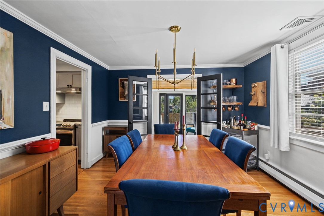 Dining room featuring wood-finish flooring, deep-tone wall paint, waist-height wainscoting, an overhead metal chandelier, and double French doors with glass panes Dining room featuring wood-finish flooring, deep-tone wall paint, waist-height wainscoting, an overhead metal chandelier, and double French doors with glass panes